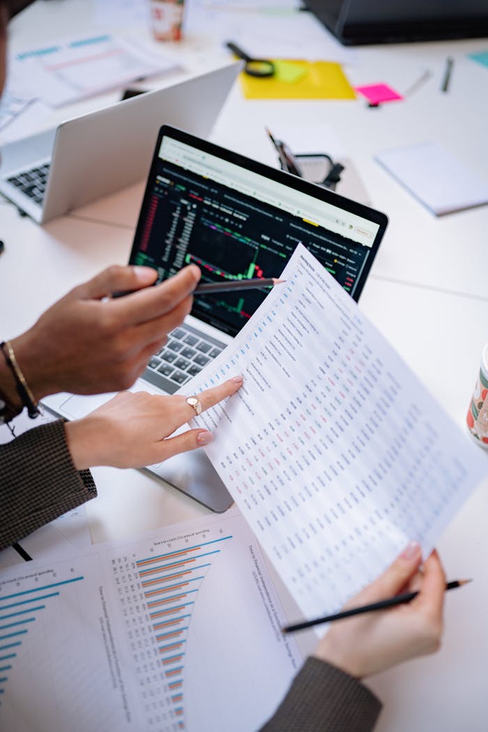 Hands holding documents analyzing data on a laptop in a collaborative office setting.